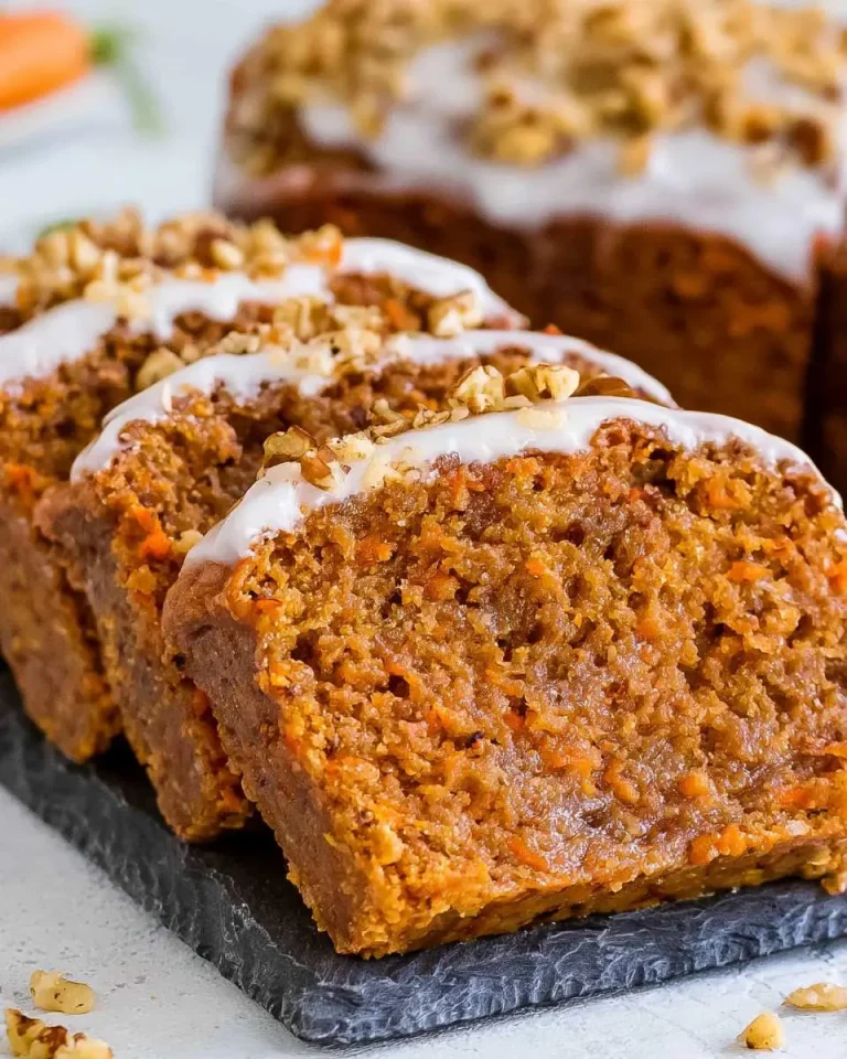 Sliced Moist Vegan Carrot Cake Loaf topped with white glaze and chopped walnuts on a slate serving board.