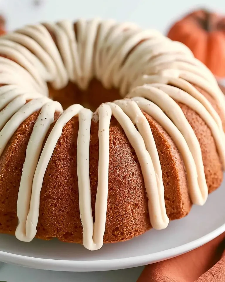 A beautifully glazed Pumpkin Bundt Cake with creamy white icing drizzled on top, displayed on a white cake stand.